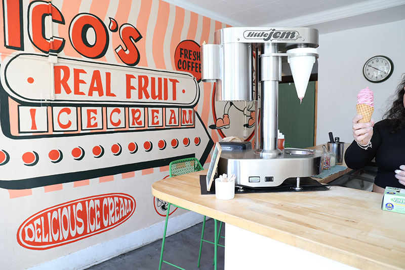 Nico%E2%80%99s+employee+finishes+making+the+ice+cream+and+hands+the+customer+a+marionberry+waffle+cone.+The+background+is+the+mural+inside+the+shop+that+fills+the+store+with+color.