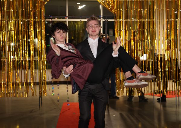 Senior Scott Cuno carries senior Connor Lanusse into the dance in his arms. Both students hold up jazz hands as they walk down the aisle. 