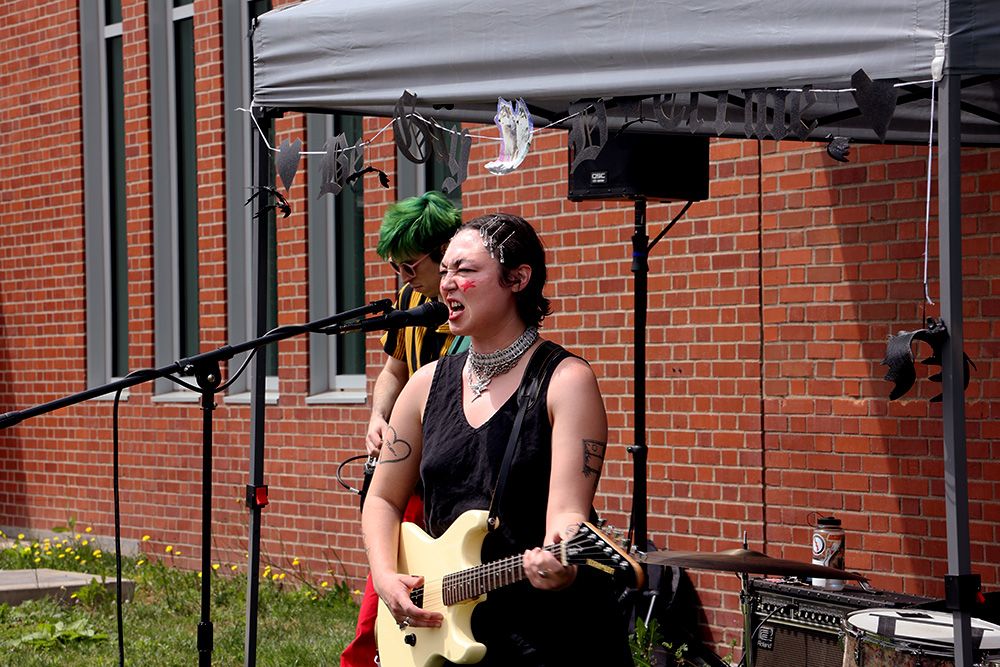 Non Binary Girlfriend’s singer Anaïs Genevieve grimaces. Their performance was moving and lots of seniors gathered around to hear them play. Genevieve pauses between songs to talk about how graduation is a big accomplishment and showed a lot of support.