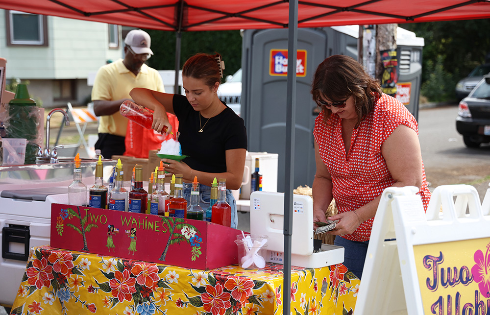 Two Wahines, a flavored shaved ice stand owned by Earl Fonville (back left), stands under a small red event tent and is decorated with a colorful yellow, red, white and blue tablecloth. They offer traditional flavors such as mango and strawberry, as well as unique flavors such as guava, passionfruit, tiger's blood and piña colada for their customers to try. Paige Wiebke stands behind the booth, making a shaved ice cone for a customer while her aunt works beside her. “We have been going to the Belmont Street Fair for 12 years,” Fonville said, and he noted how he loves feeling like a part of the community while at the fair. He hopes to maintain this feeling of community in the years to come. 