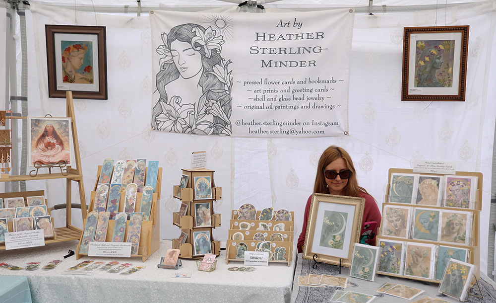 Heather Sterling-Minder sits at a table inside the booth that represents her company called Art By Heather Sterling-Minder. She mainly focuses on selling prints, cards, bookmarks, stickers, and other gift items, which you can also look at on her instagram @heather.sterlingminder. Surrounding her are examples of her artwork for sale. “I really enjoy events like this that really bring the community together,” Sterling-Minder said. In addition to this, she mentioned how she loves the music played by live bands and local musicians, as well as getting to see returning vendors at their booths. 