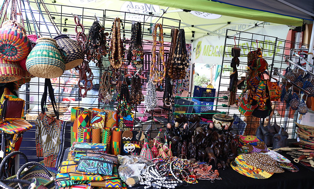 A large table topped with traditional wallets, wood carvings and vibrant drums is displayed for the public to see inside Ward’s booth. Colorful baskets, bags and necklaces adorn a rack, located on the back of the table. 