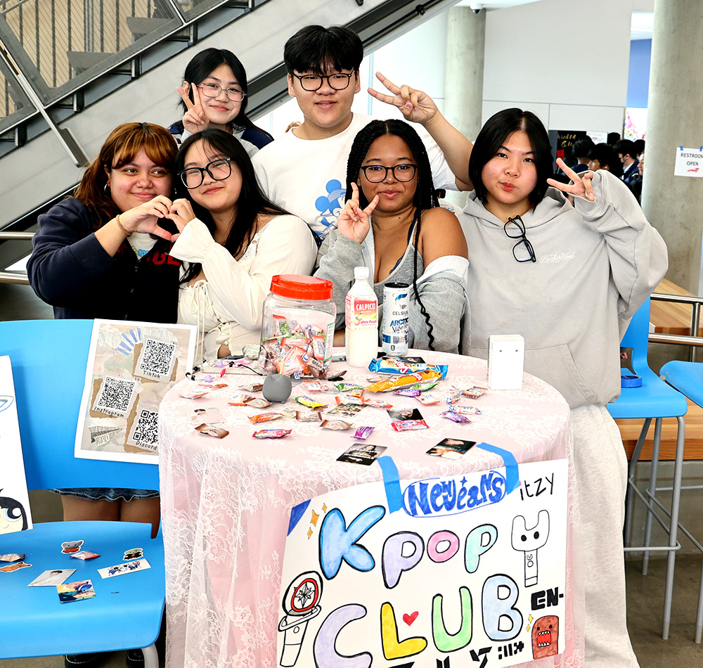 K-Pop Club poses by their table at the club fair with hearts and peace signs. Junior Queenie Chen (right), president of K-Pop Club, states that McDaniel can look forward to their performances at the multicultural assembly along with by the stairs in the commons at lunch.