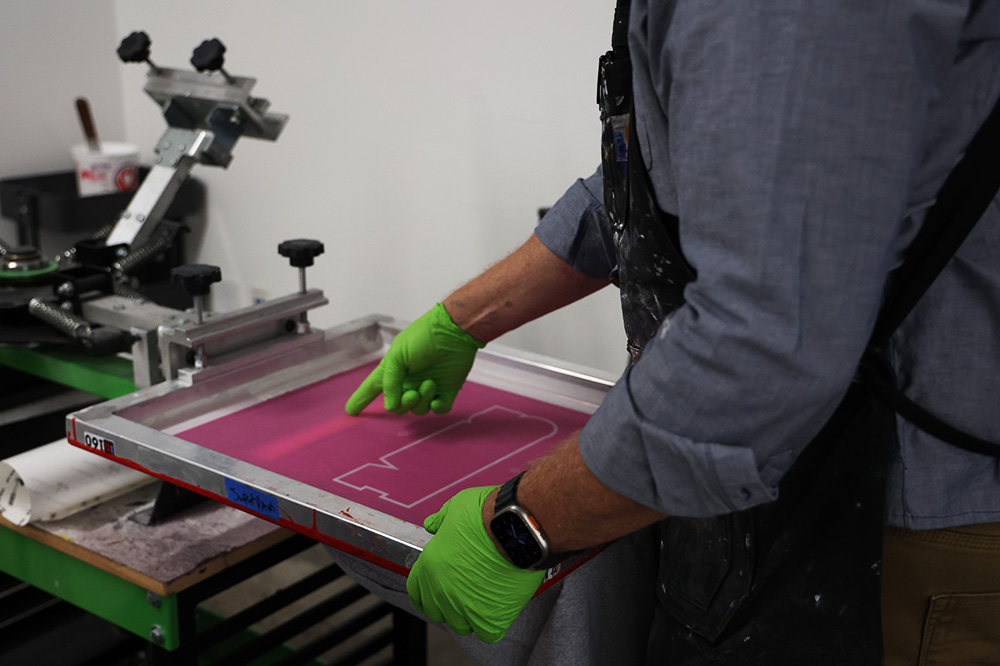 Printshop teacher Randy Maves registers a screen to line up for printing. This screen is for MHS sweatpants that are sold at the student store.