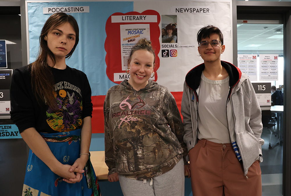 The Literary magazine program and Podcasting Network come together. Evangeline Johnson (far right), Casey Coleman (middle) and Sureika Shore (far left). They stand in front of a board that showcases their media outlets.