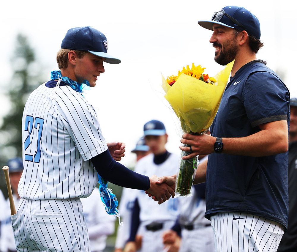 Senior Jack Burrell shakes the hand of coach Chase Franks. Coach Franks is holding a bouquet of flowers for Burrell's mom, a gesture that was repeated for all senior moms on the team.