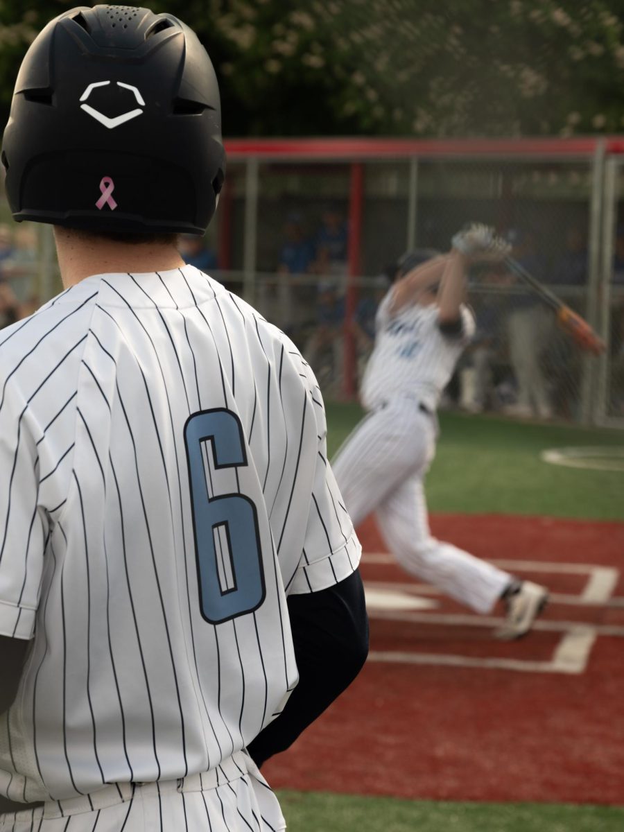 Ruona-Banister looks over at Jackson De Young while he’s up at bat. He has a dedicated batter's-circle to warm up while waiting for De Young to hit, strike out or walk.
