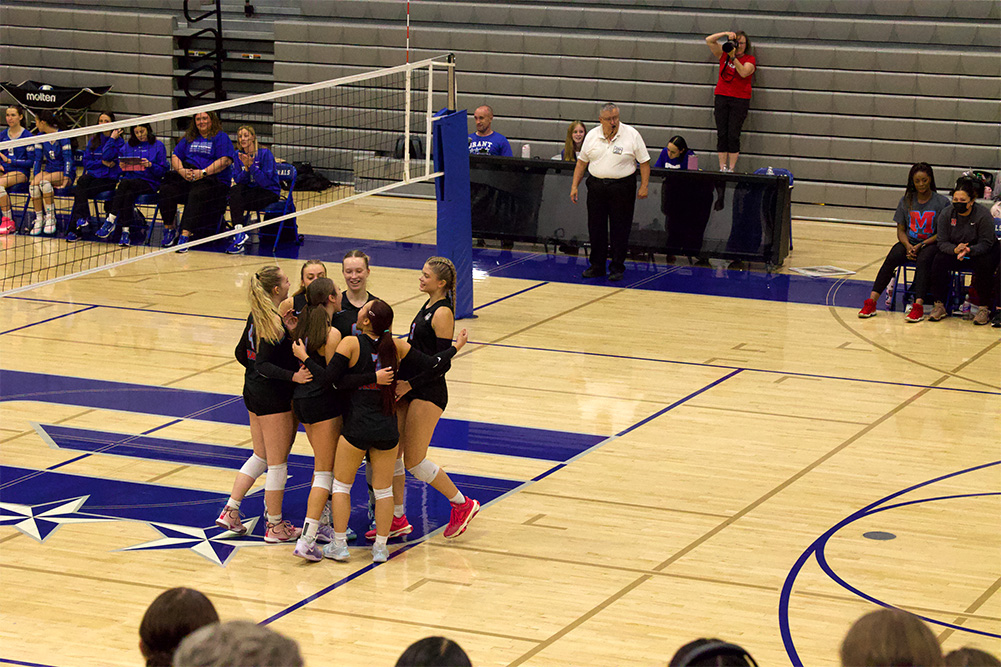 McDaniel joins a huddle after scoring a point. The players gathered at center court to celebrate. They had a close first set against Grant.
