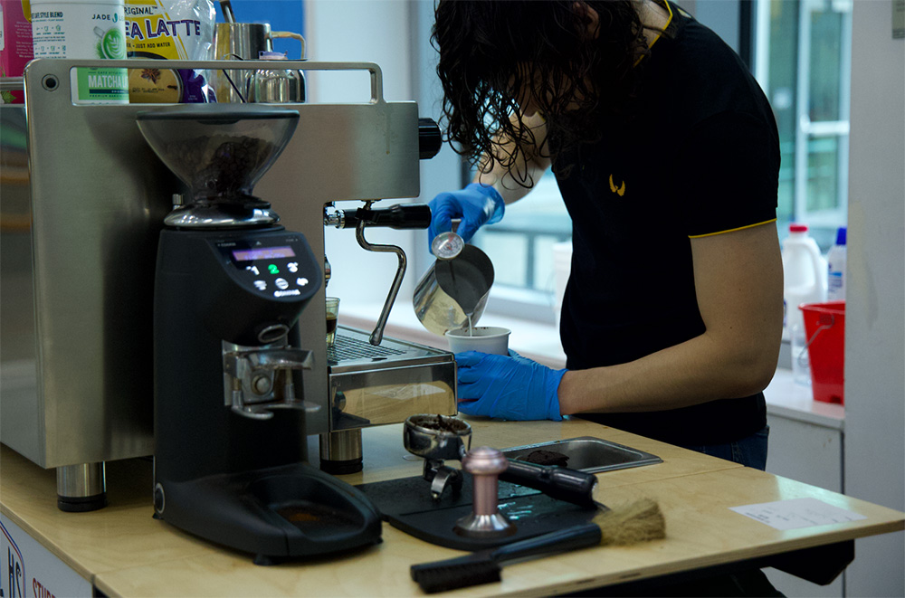 Latte artist and student Daniel Zuniga-Reyes creates orders before class. The coffee cart also does direct drink deliveries to classrooms.